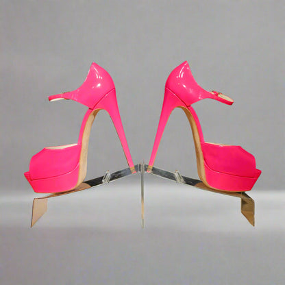 Pair of bright pink high-heeled shoes on a reflective stand against a gray background