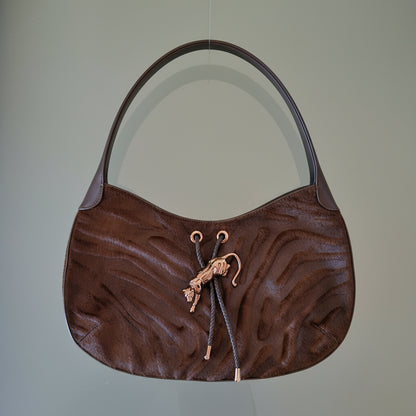 Brown textured handbag with decorative elements on a light gray background