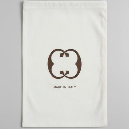 Brown leather bag on a glass table with a white pouch featuring a logo.