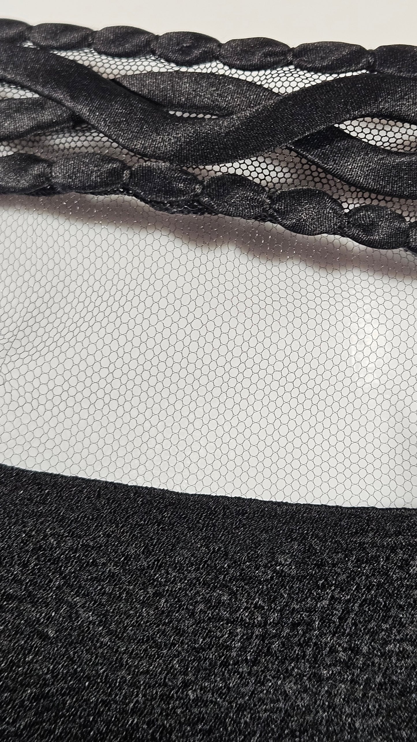 Close-up of a textured black fabric with braided pattern on a neutral background