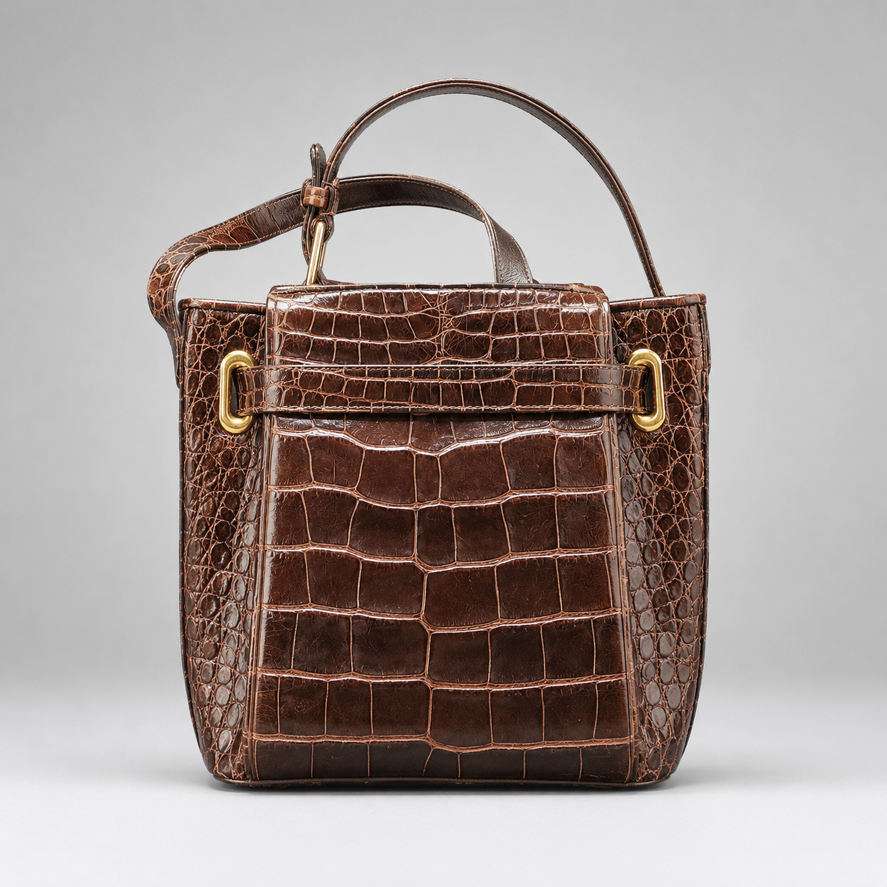 Brown crocodile skin handbag with gold hardware on a light gray background