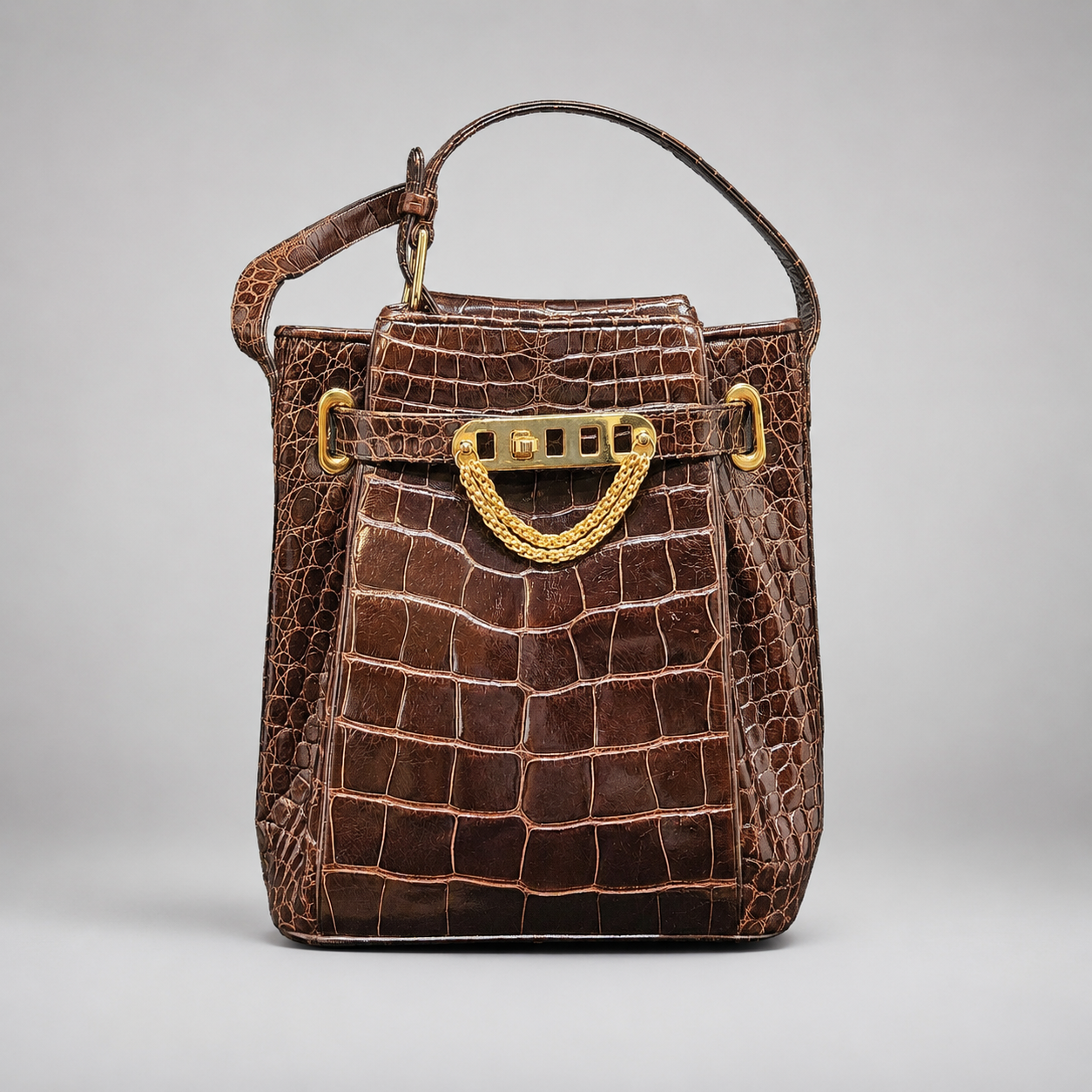 Brown crocodile skin handbag with gold hardware on a light gray background