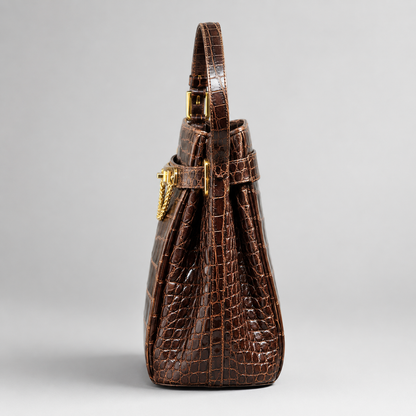 Brown crocodile skin handbag with gold hardware on a light gray background