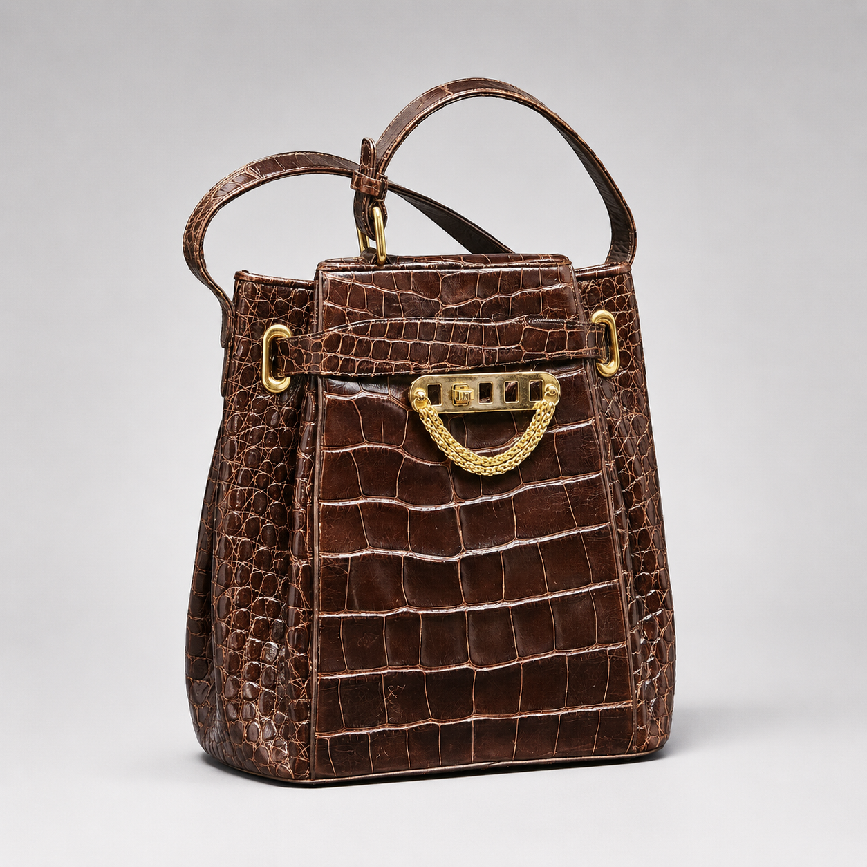 Brown crocodile skin handbag with gold hardware on a light gray background