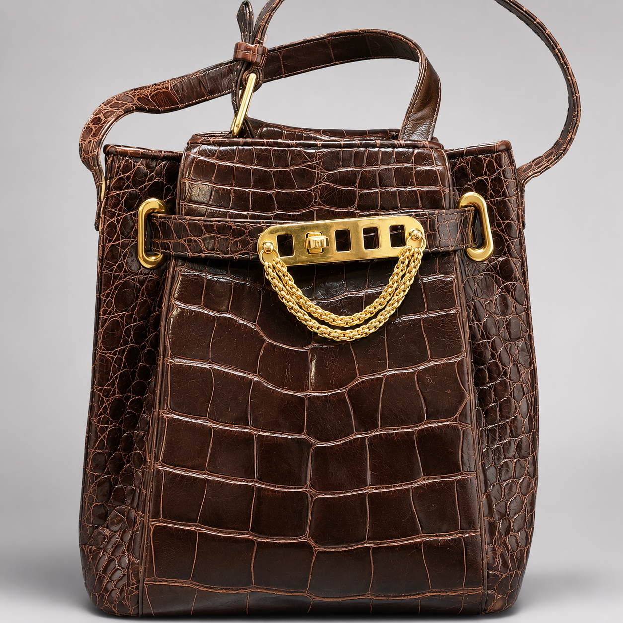 Brown crocodile skin handbag with gold hardware on a gray background