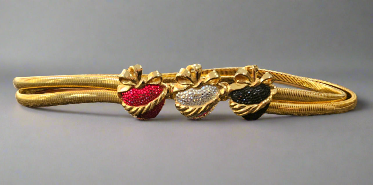 Gold belt with red, silver, and black heart-shaped stones on a gray background