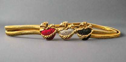 Gold belt with red, silver, and black heart-shaped stones on a gray background