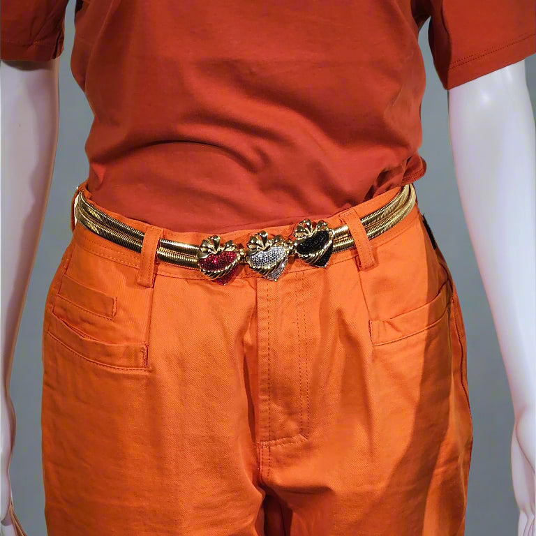 Person wearing an orange outfit with a gold belt featuring heart-shaped charms on a gray background