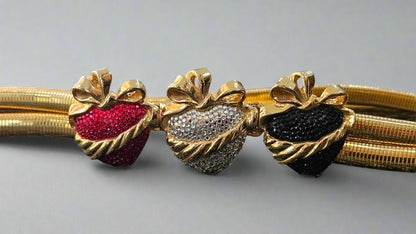 Gold belt with red, silver, and black heart-shaped gemstones on a light gray background