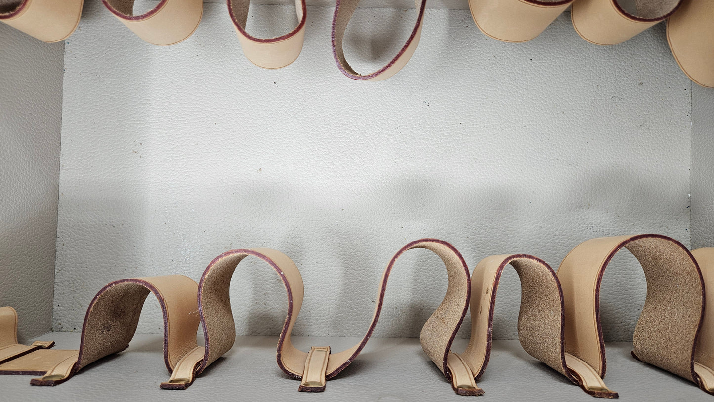 Row of beige and brown leather shoe lasts on a gray surface with a white wall background.