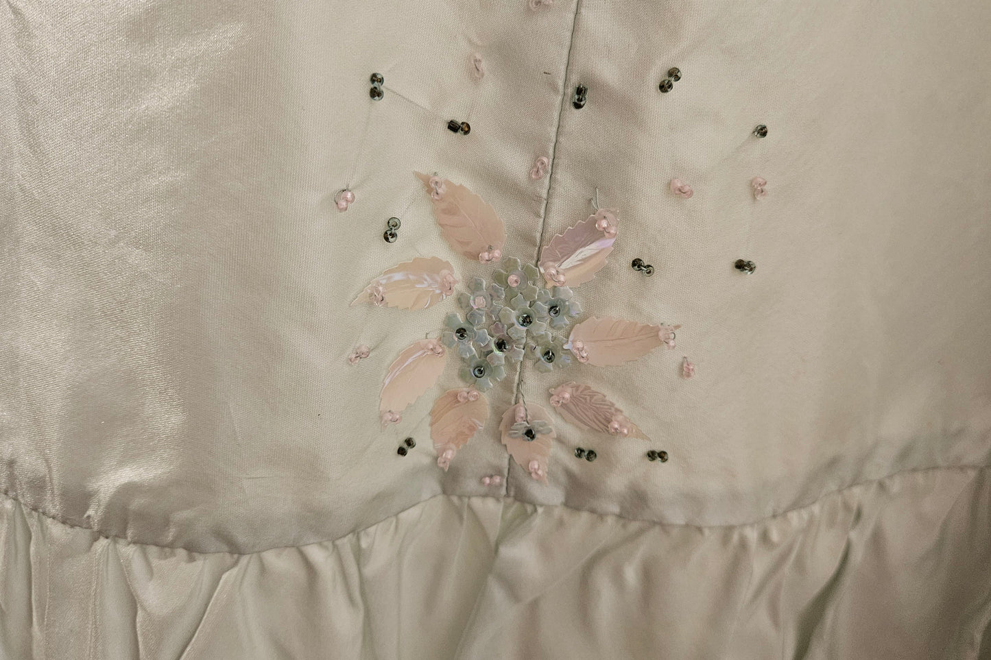 Close-up of a satin fabric with floral embroidery and bead details.