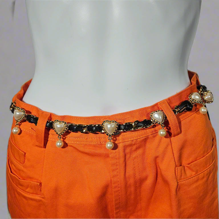 Orange pants with a decorative belt featuring pearls and heart-shaped charms on a plain background.