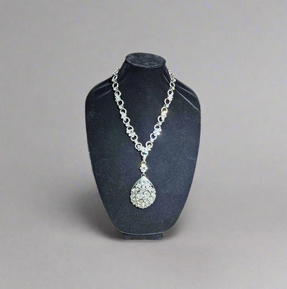 Silver necklace with a pendant on a black stand against a wooden background
