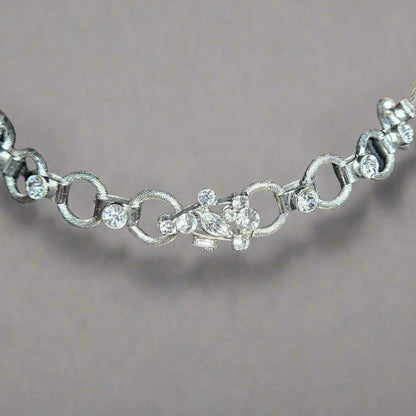 Silver necklace latch with clear stones on a black velvet stand against a blurred background