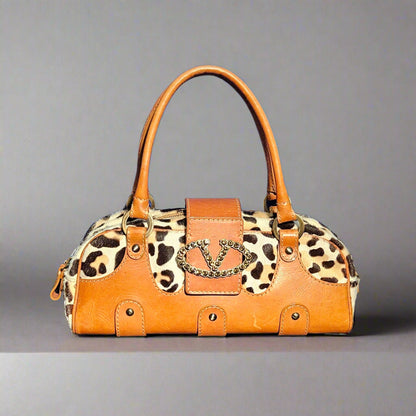 Leopard print handbag with brown leather accents on a gray background