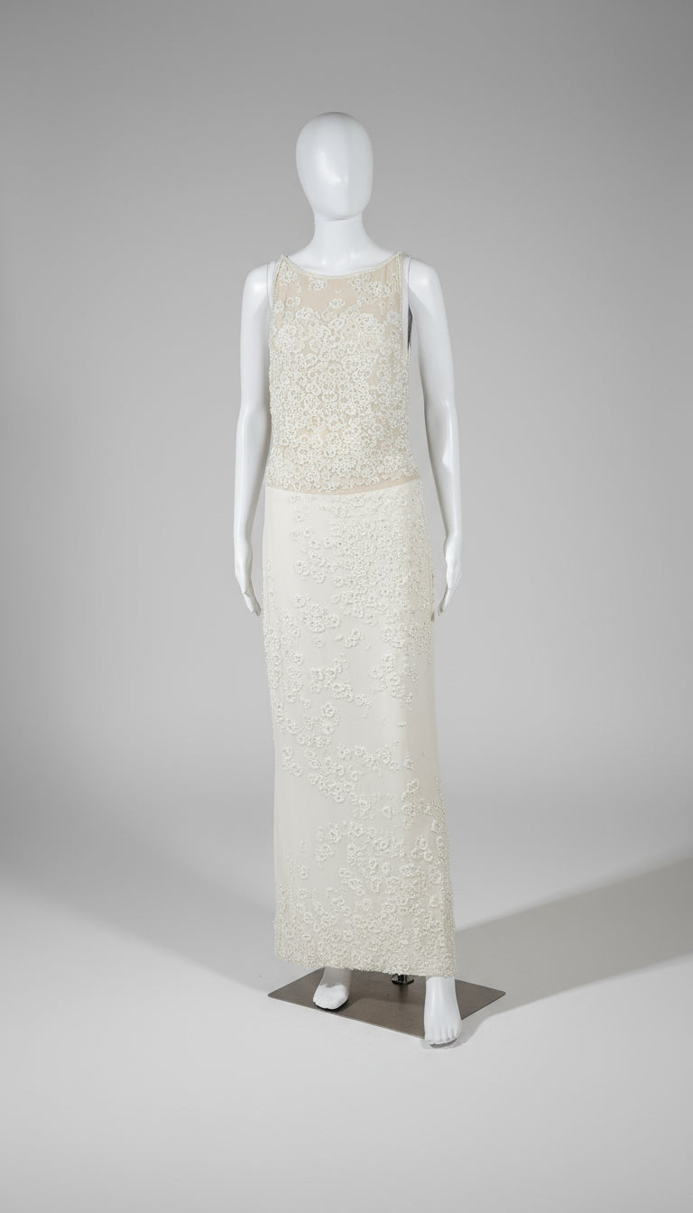 Mannequin wearing a long, light-colored dress on a plain background