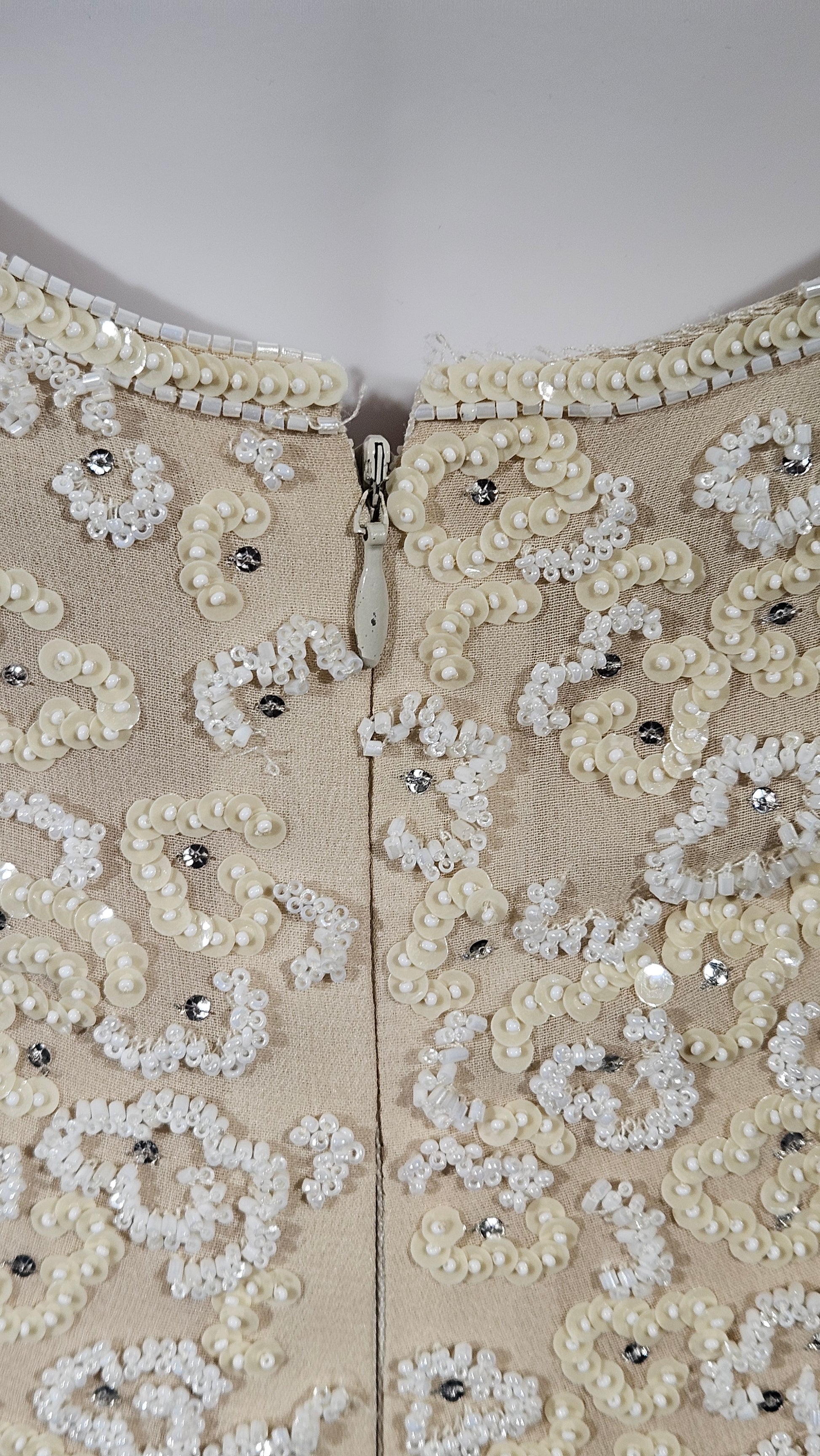 Beige fabric with intricate white lace and bead detailing on a plain background