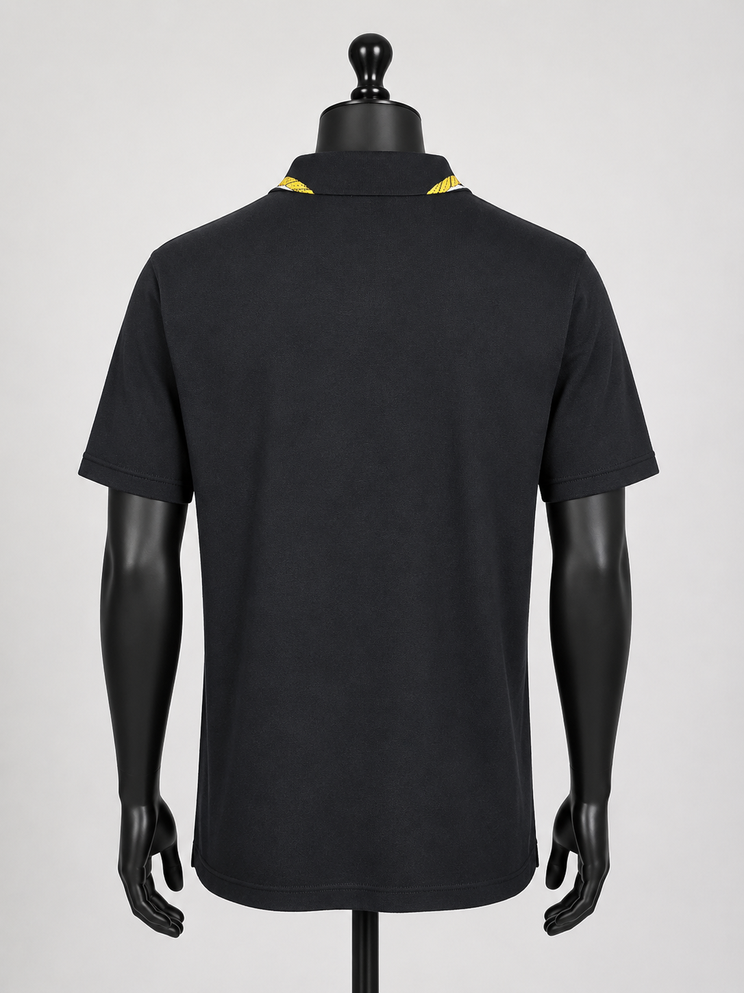 Black polo shirt on a mannequin with yellow accents against a gray background
