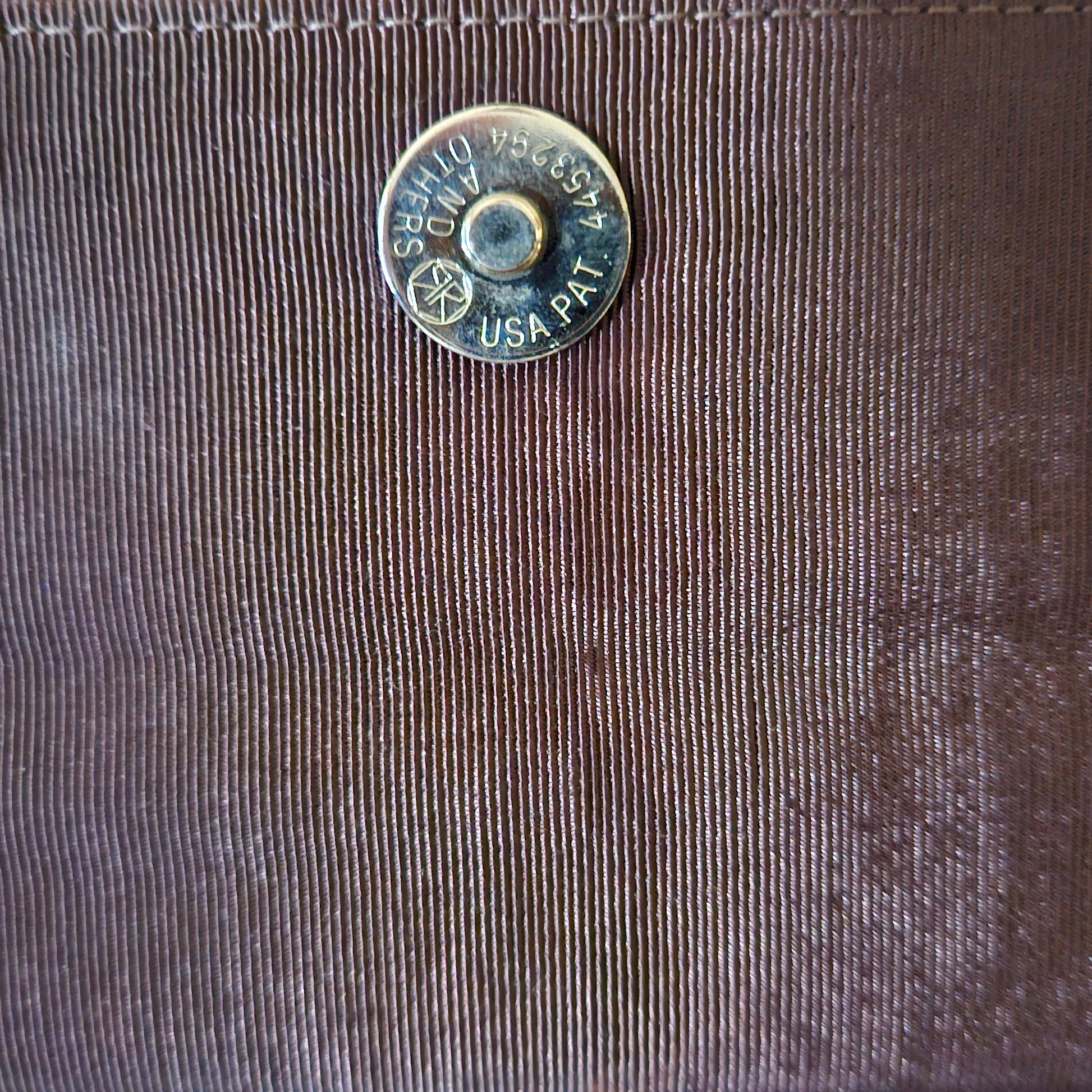 Close-up of a bag interior flap with a metal button featuring text on it.