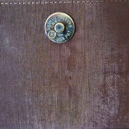 Close-up of a bag interior flap with a metal button featuring text on it.
